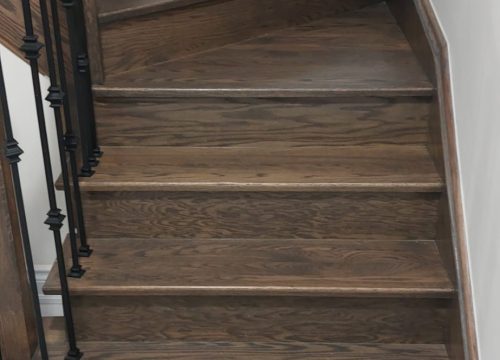 Staircase renovated with sleek modern metal pickets and rich wood staining, creating a timeless and luxurious look.